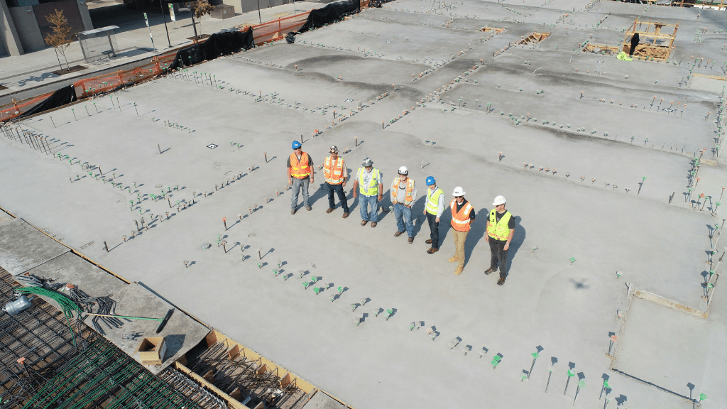 7 subcontractors standing on a construction site with a newly poured foundation